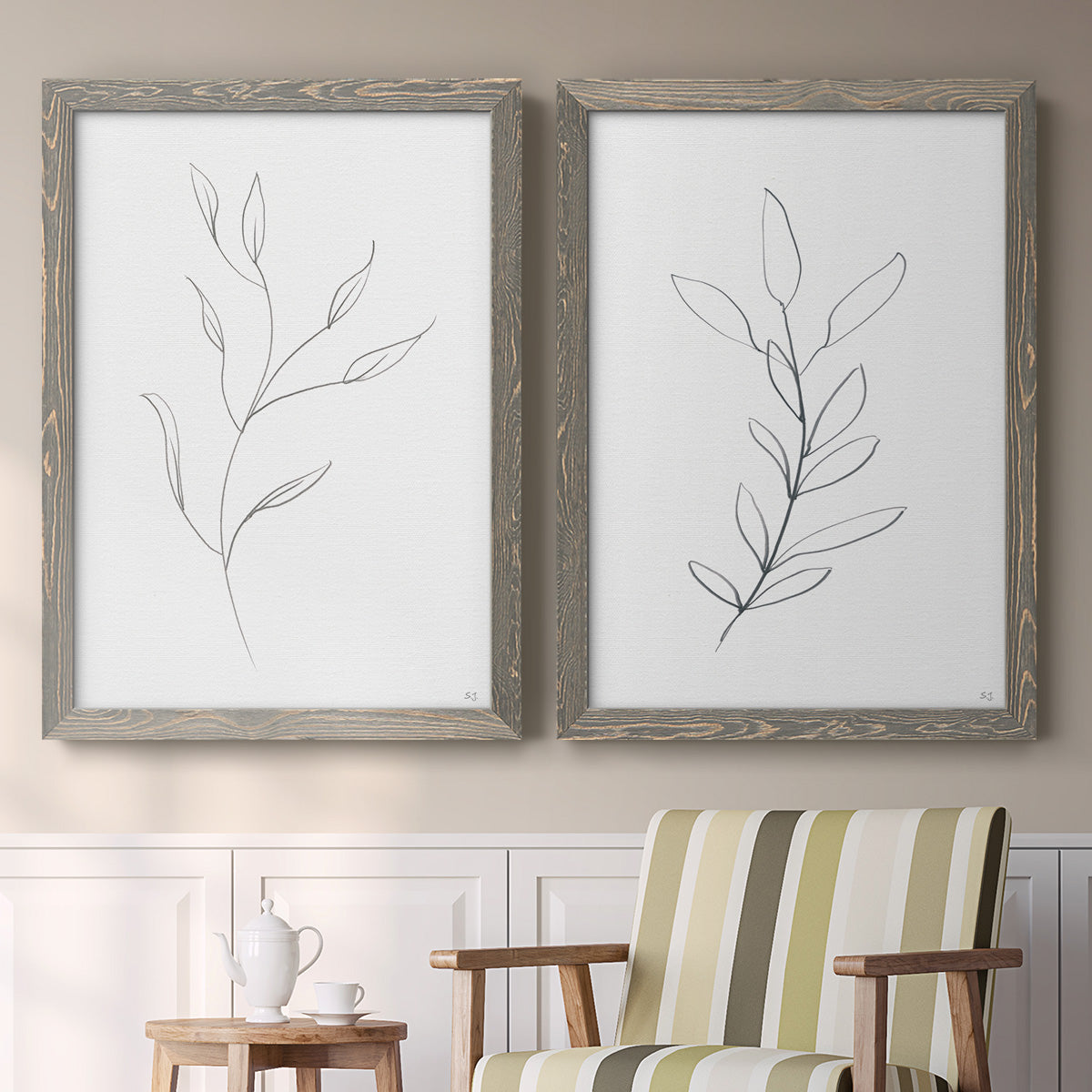 Set of two gray barnwood framed canvas prints depicting two minimalist botanical line drawings featuring single continuous-line leafy branches above a sideboard in a cozy sitting room.