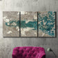 Three-panel canvas wall art featuring layered mineral abstract textures, displayed in a living room above a suede accent chair.