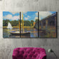 Three-panel canvas wall art featuring bridge crossing river landscape, displayed in a living room above a suede accent chair.