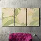 Three-panel canvas wall art featuring minimal verdant floral abstraction, displayed in a living room above a suede accent chair.