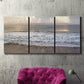 Three-panel canvas wall art featuring calm coastal shoreline seascape, displayed in a living room above a suede accent chair.