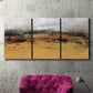 Three-panel canvas wall art featuring abstract bridge landscape in ochre, displayed in a living room above a suede accent chair.