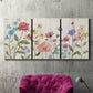 Three-panel canvas wall art featuring delicate wildflower illustration, displayed in a living room above a suede accent chair.