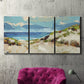 Three-panel canvas wall art featuring sand dunes beside open water, displayed in a living room above a suede accent chair.