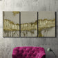 Three-panel canvas wall art featuring gold accented abstract ravine, displayed in a living room above a suede accent chair.