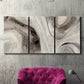 Three-panel canvas wall art featuring layered stone inspired abstract forms, displayed in a living room above a suede accent chair.