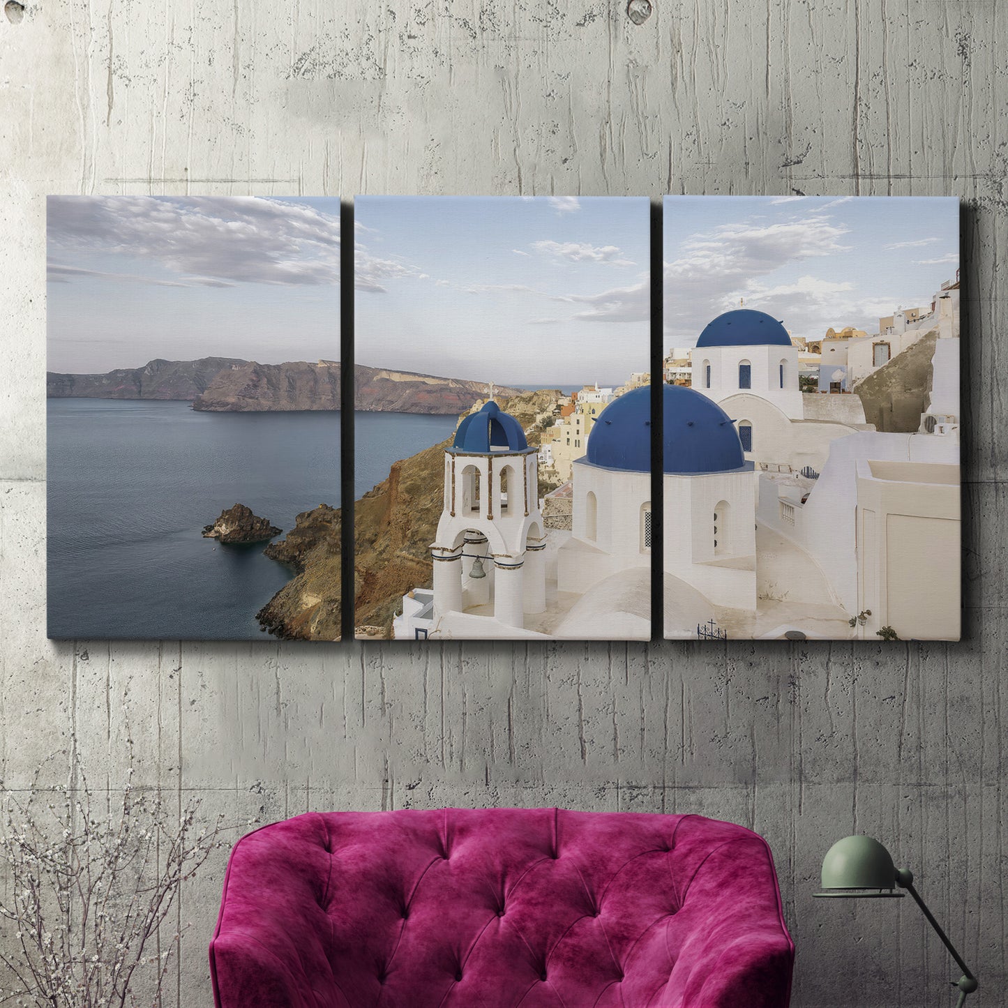 Three-panel canvas wall art featuring white buildings overlooking sea cliffs, displayed in a living room above a suede accent chair.