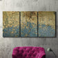Three-panel canvas wall art featuring metallic abstract gold tones, displayed in a living room above a suede accent chair.