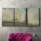 Three-panel canvas wall art featuring tall abstract tree form, displayed in a living room above a suede accent chair.