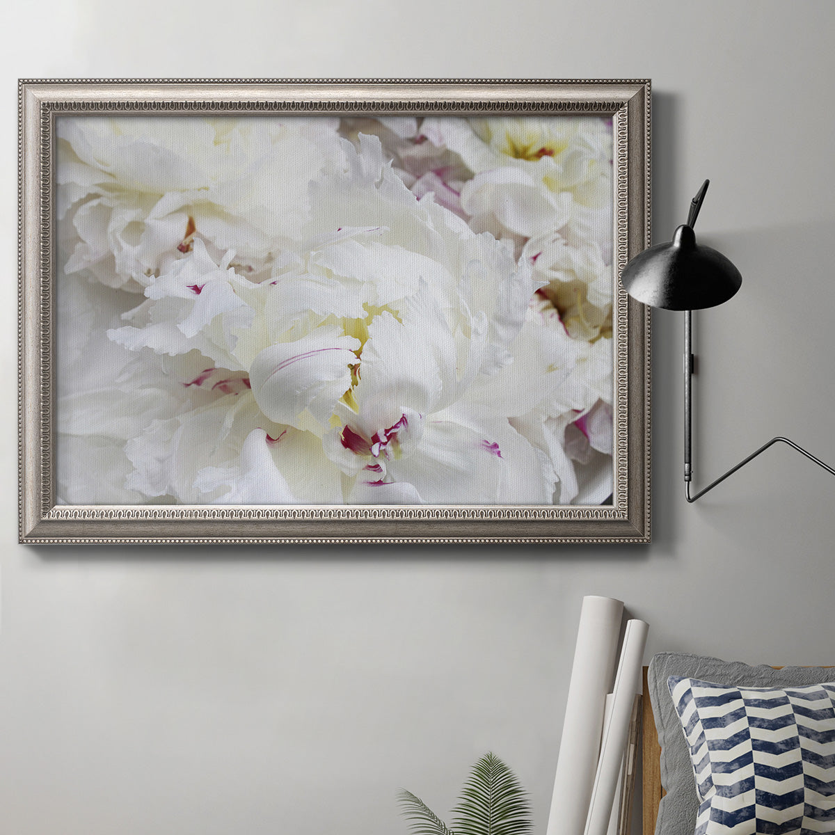 White peonies in bloom in an ornate vintage silver frame displayed in a neutral interior setting.