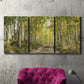 Three-panel canvas wall art featuring tree lined forest road photograph, displayed in a living room above a suede accent chair.