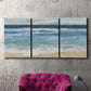 Three-panel canvas wall art featuring rolling ocean waves near shore, displayed in a living room above a suede accent chair.
