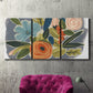 Three-panel canvas wall art featuring colorful botanical illustration, displayed in a living room above a suede accent chair.