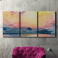 Three-panel canvas wall art featuring prismatic watercolor coastal seascape, displayed in a living room above a suede accent chair.