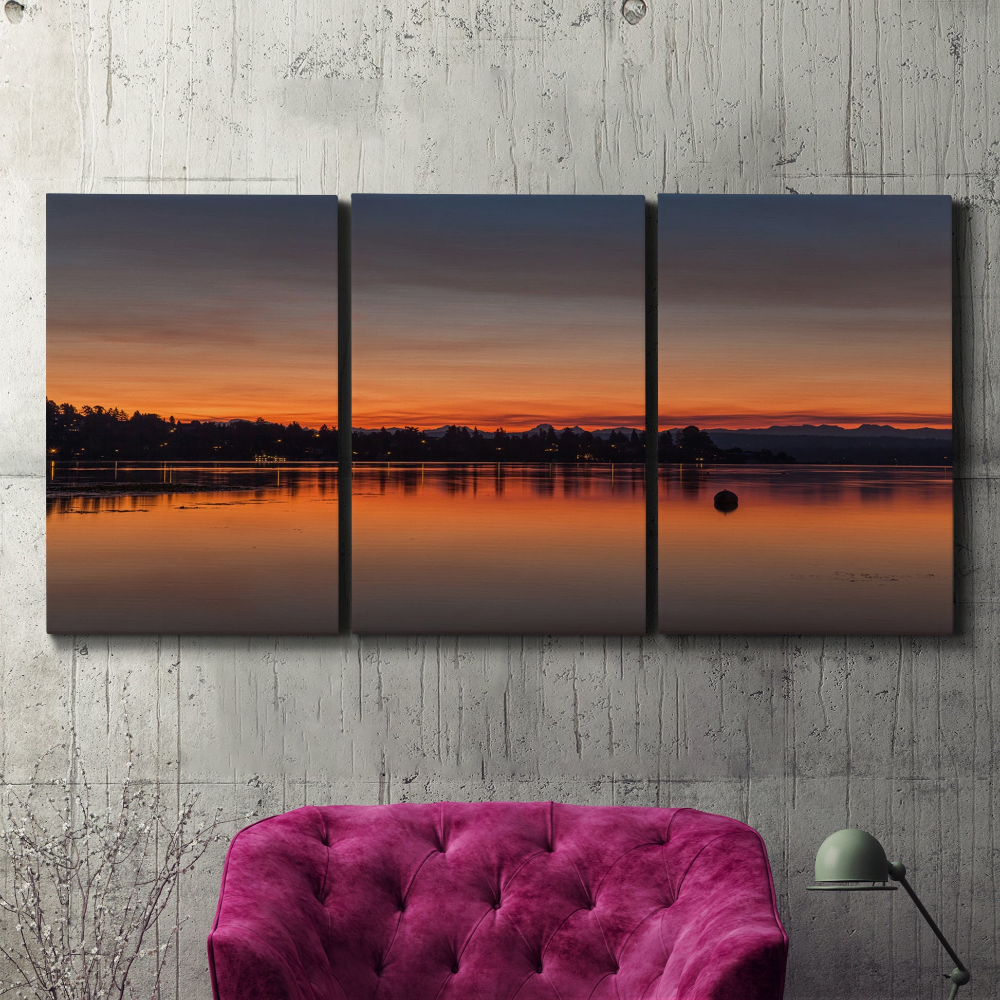 Three-panel canvas wall art featuring glowing sunset over water, displayed in a living room above a suede accent chair.