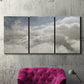 Three-panel canvas wall art featuring aerial landscape view photograph, displayed in a living room above a suede accent chair.