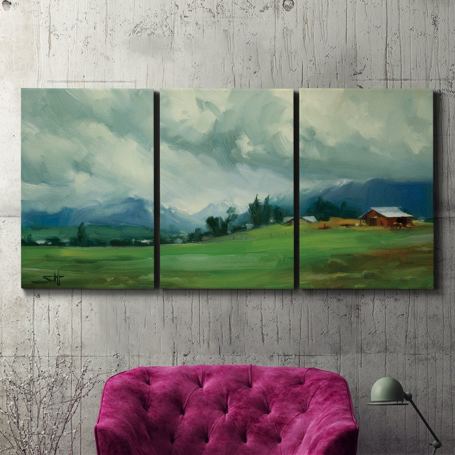 Three-panel canvas wall art featuring wide pastoral valley landscape, displayed in a living room above a suede accent chair.