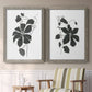 Set of two gray barnwood framed canvas prints depicting two minimalist botanical prints featuring black leafy vine silhouettes above a sideboard in a cozy sitting room.