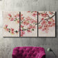 Three-panel canvas wall art featuring blooming cherry blossom branches, displayed in a living room above a suede accent chair.