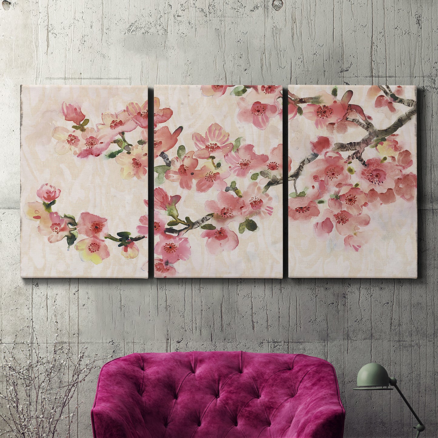 Three-panel canvas wall art featuring blooming cherry blossom branches, displayed in a living room above a suede accent chair.