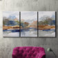 Three-panel canvas wall art featuring layered abstract mountain forms, displayed in a living room above a suede accent chair.