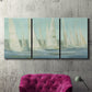 Three-panel canvas wall art featuring sailboats silhouetted at sunrise, displayed in a living room above a suede accent chair.