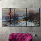 Three-panel canvas wall art featuring snow covered road leading to village, displayed in a living room above a suede accent chair.