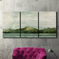 Three-panel canvas wall art featuring riverbank watercolor landscape, displayed in a living room above a suede accent chair.