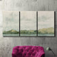 Three-panel canvas wall art featuring riverbank landscape with trees, displayed in a living room above a suede accent chair.