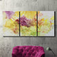 Three-panel canvas wall art featuring abstract floral rhythm composition, displayed in a living room above a suede accent chair.