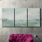 Three-panel canvas wall art featuring soft abstract coastal tones, displayed in a living room above a suede accent chair.