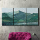 Three-panel canvas wall art featuring muted mountain range in grey tones, displayed in a living room above a suede accent chair.