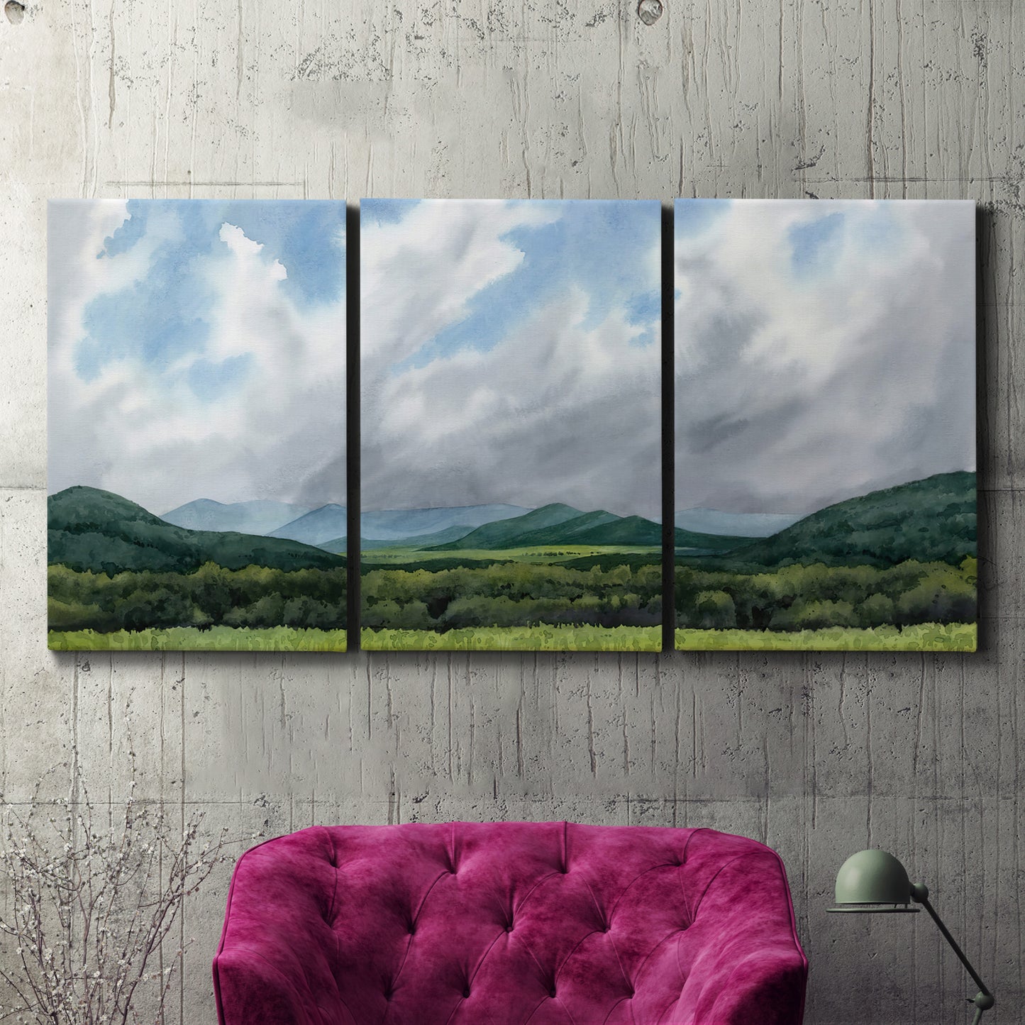 Three-panel canvas wall art featuring pastoral mountain landscape in blue, displayed in a living room above a suede accent chair.