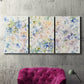 Three-panel canvas wall art featuring flowing abstract watercolor, displayed in a living room above a suede accent chair.