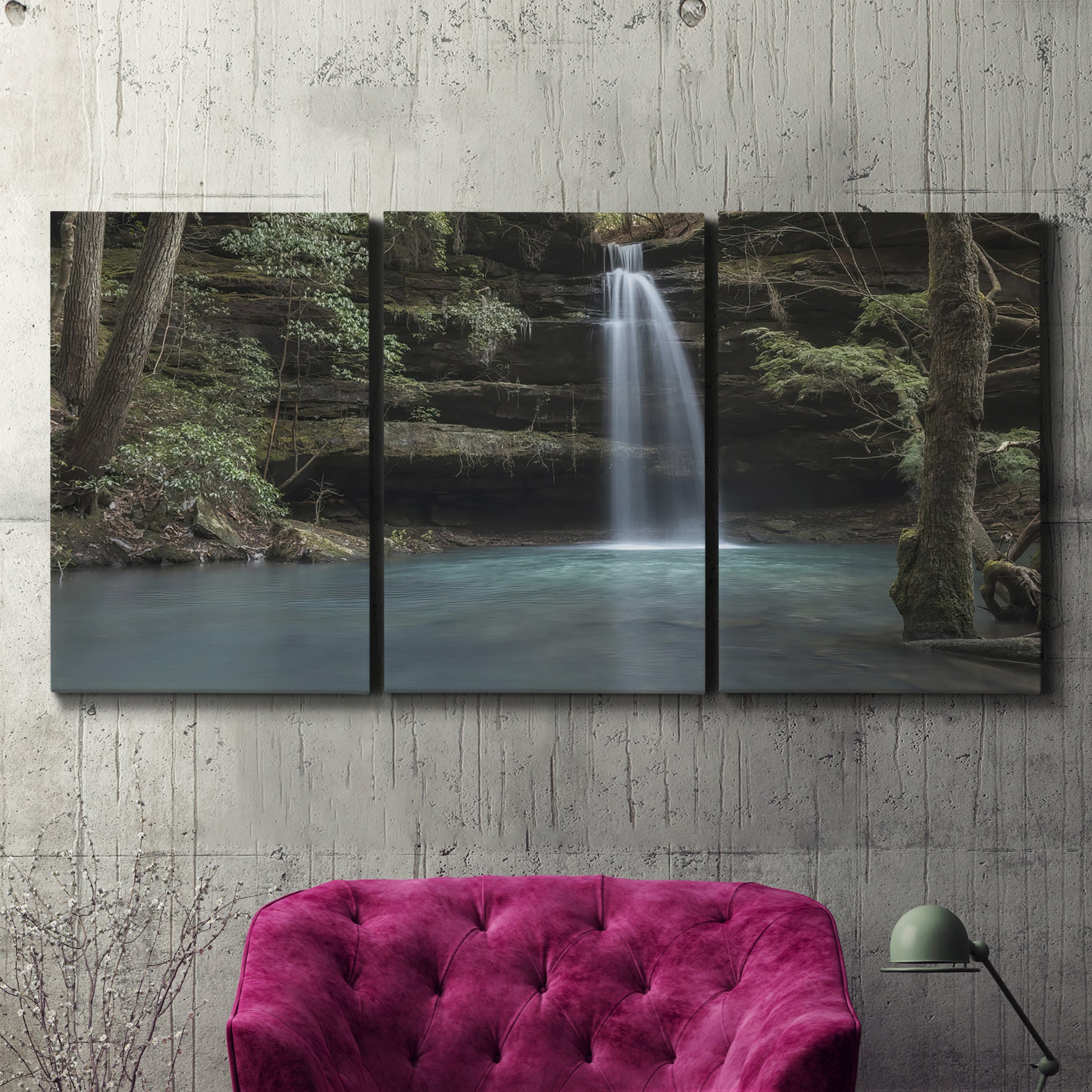 Three-panel canvas wall art featuring waterfall cascading through forest, displayed in a living room above a suede accent chair.