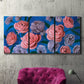 Three-panel canvas wall art featuring layered botanical petal abstractions, displayed in a living room above a suede accent chair.