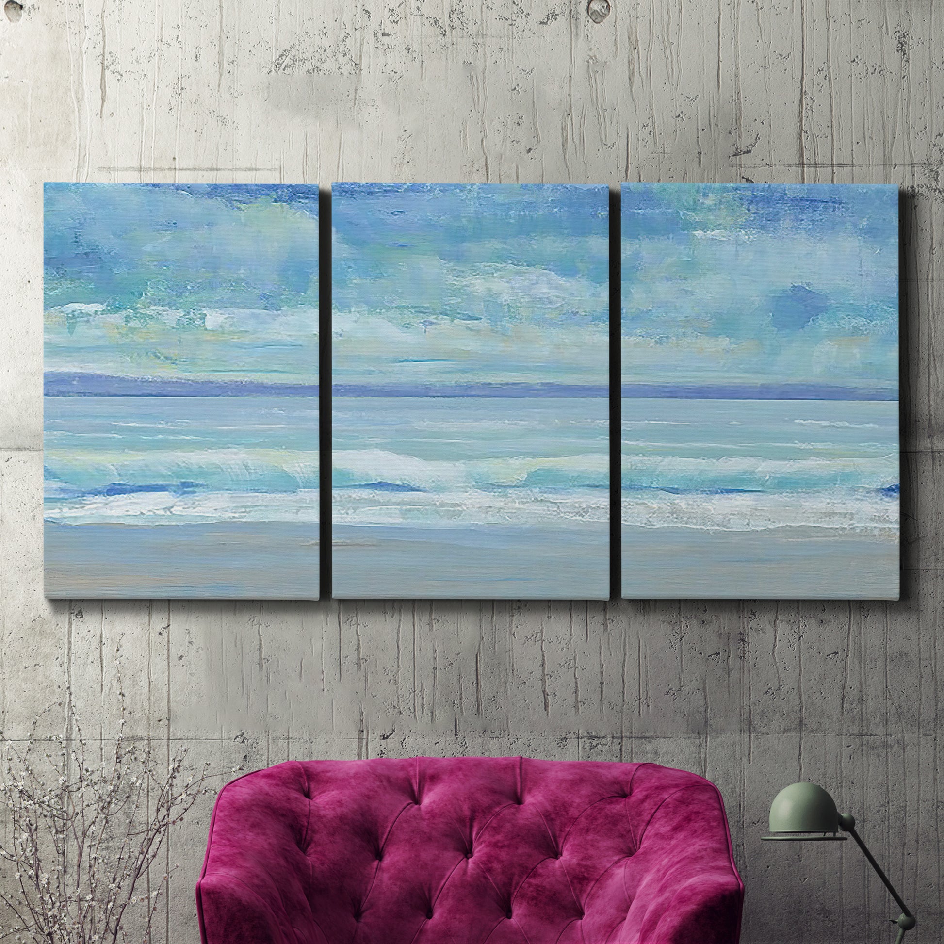 Three-panel canvas wall art featuring rolling ocean surf along shoreline, displayed in a living room above a suede accent chair.
