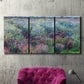 Three-panel canvas wall art featuring flowered riverbank with trees, displayed in a living room above a suede accent chair.