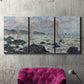 Three-panel canvas wall art featuring rough seas along rocky coast, displayed in a living room above a suede accent chair.