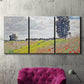 Three-panel canvas wall art featuring open poppy field in countryside, displayed in a living room above a suede accent chair.