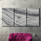 Three-panel canvas wall art featuring minimal monochrome abstract forms, displayed in a living room above a suede accent chair.