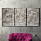 Three-panel canvas wall art featuring grid based geometric abstraction, displayed in a living room above a suede accent chair.