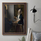 Quiet interior genre scene of a woman with scales by Johannes Vermeer in an ornate bronzed mahogany wood frame displayed in a neutral interior setting.