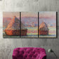 Three-panel canvas wall art featuring winter grainstacks glowing at sunset, displayed in a living room above a suede accent chair.