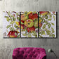 Three-panel canvas wall art featuring apples hanging from branch, displayed in a living room above a suede accent chair.