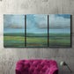 Three-panel canvas wall art featuring wide valley landscape with rolling hills, displayed in a living room above a suede accent chair.