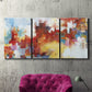 Three-panel canvas wall art featuring abstract city lights composition, displayed in a living room above a suede accent chair.
