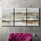 Three-panel canvas wall art featuring layered turquoise and earth tones abstract, displayed in a living room above a suede accent chair.