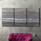 Three-panel canvas wall art featuring shoreline between land and sea, displayed in a living room above a suede accent chair.