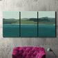 Three-panel canvas wall art featuring calm lake water under open sky, displayed in a living room above a suede accent chair.